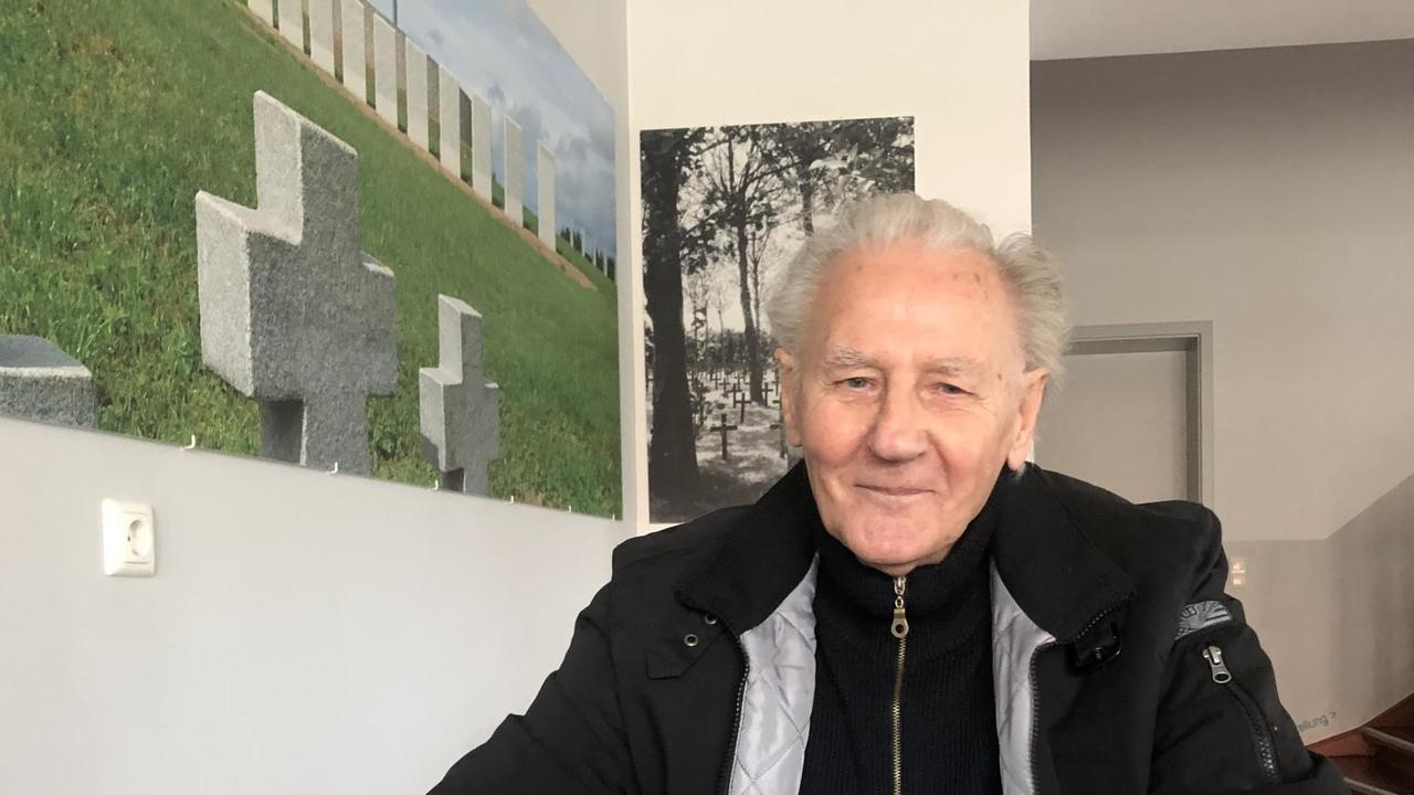 Willi Lehmann mit einer Brille in der Hand an einem Tisch sitzend und in die Kamera lächelnd