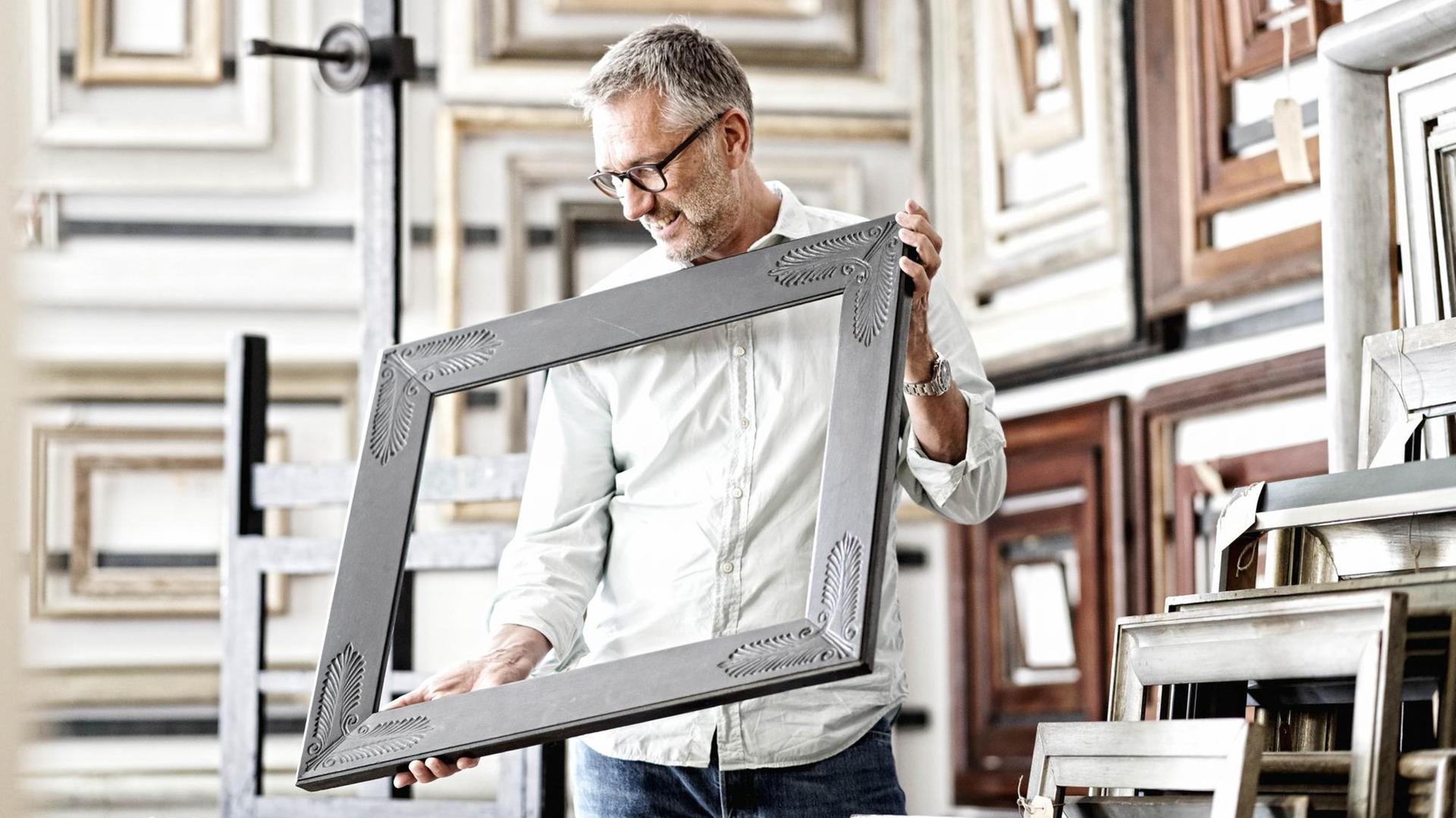 Werner Murrer in seinem Atelier mit einem Bilderrahmen in der Hand. Werner Murrer in seinem Atelier mit einem Bilderrahmen in der Hand.
