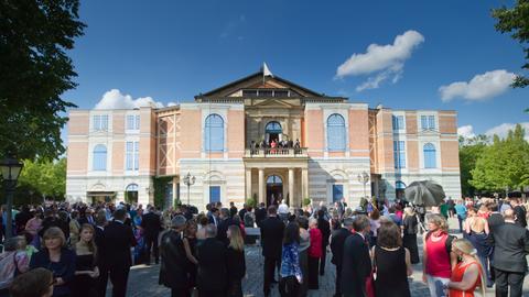Besucher warten am 25.07.2014 bei der Eröffnung der Bayreuther Festspiele auf dem Grünen Hügel in Bayreuth (Bayern) bei einer unplanmäßigen Unterbrechung wegen eines technischen Defekts vor dem Festspielhaus.