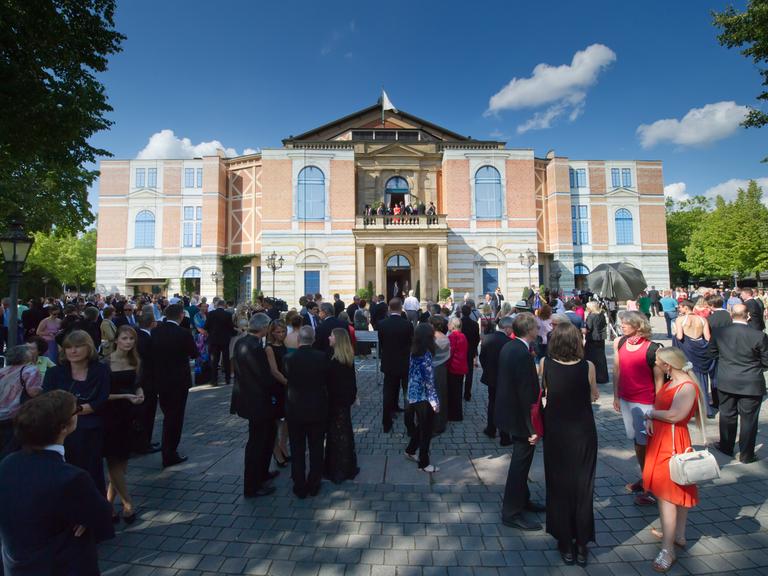 Besucher warten am 25.07.2014 bei der Eröffnung der Bayreuther Festspiele auf dem Grünen Hügel in Bayreuth (Bayern) bei einer unplanmäßigen Unterbrechung wegen eines technischen Defekts vor dem Festspielhaus.