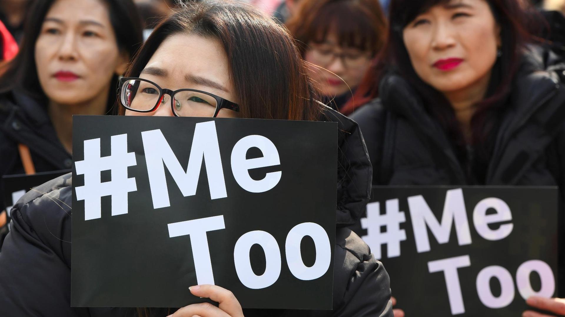 Das Bild zeigt Frauen in Südkorea, die schwarze Plakate mit weißer Schrift "#MeToo" hochhalten. 