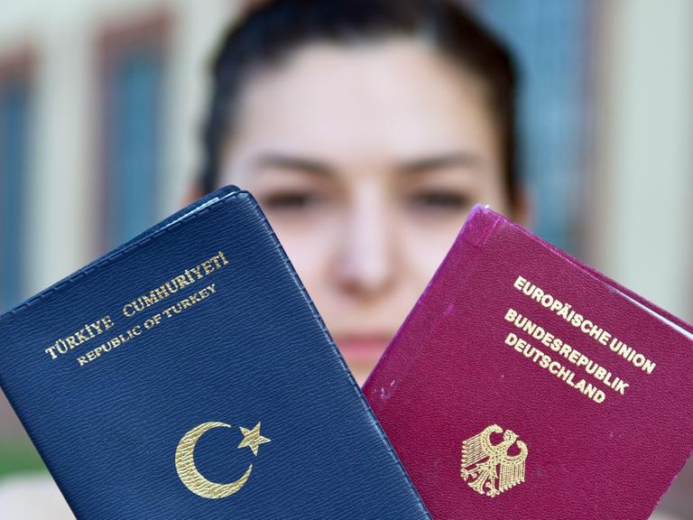 Eine junge Frau hält einen türkischen und einen deutschen Reisepass in den Händen.