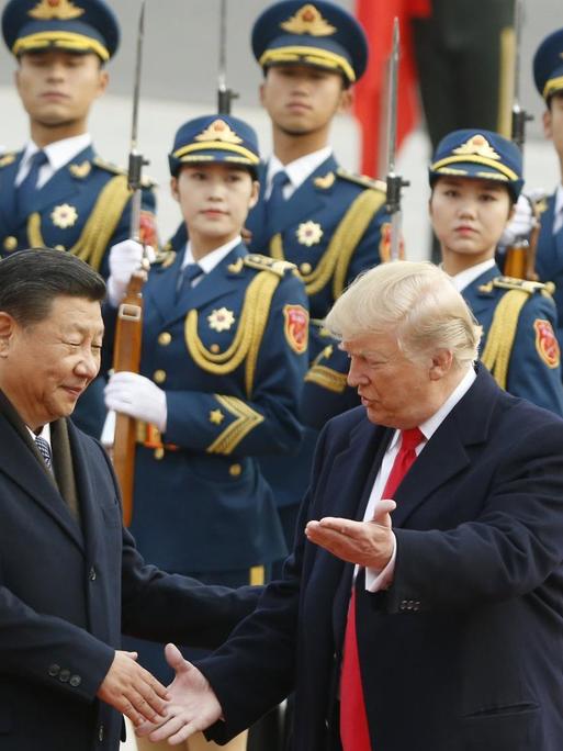 Xi Jinping begrüßt Donald Trump während einer Zeremonie in Peking 2017, im Hintergrund stehen Soldaten Spalier.
