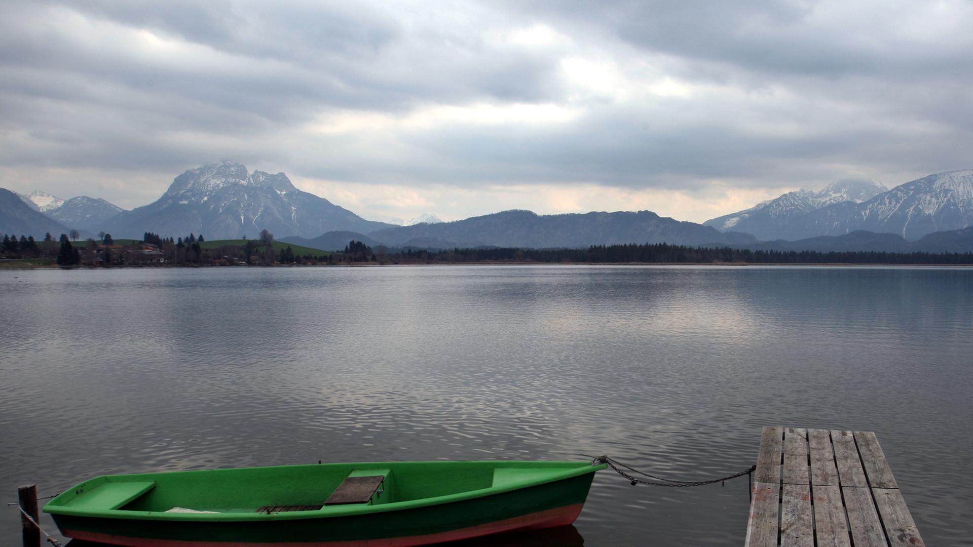 Wolkenverhangen ist es über einem See auf dem ein Holzboot an einem Steg liegt.