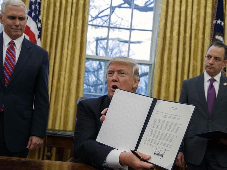 US-Präsident Donald Trump (m.) mit dem Dektret zum Ausstieg aus dem Handelsabkommen TPP. Links ist Vize-Präsident Mike Pence, rechts ist der Stabschef im Weißen Haus, Reince Priebus, zu sehen.