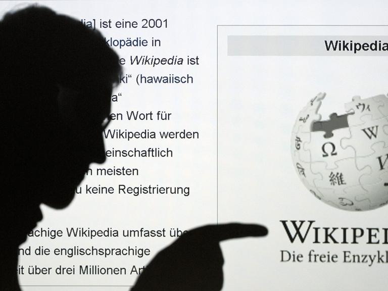Die Silhouette eines Mannes, der mit seinem Finger auf das Wort Wikipedia zeigt, ist vor der Internetseite der Online-Enzyklopädie Wikipedia zu sehen.