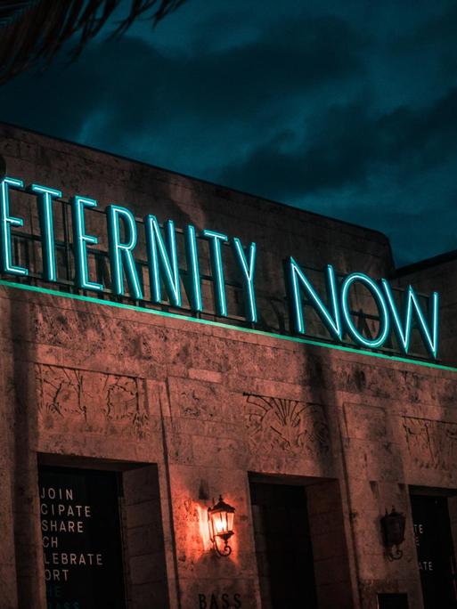 Gebäude bei Nacht mit Leuchtschrift "Eternity now"