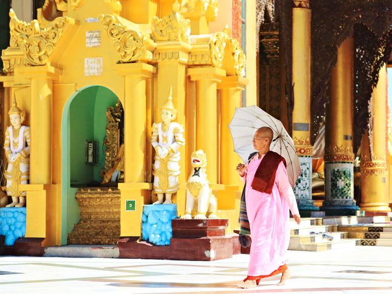 Eine Nonne mit Regenschirm (Sonnenschirm) geht durch die Shwedagon Pagode in der Stadt Yangon in Myanmar.