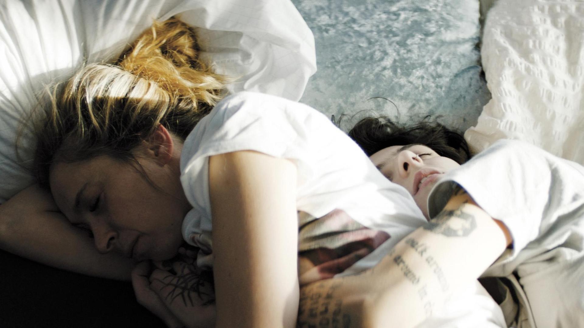 Zwei Personen liegen schlafend, Arm in Arm im Bett