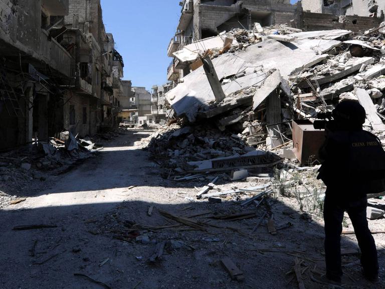 Ein Journalist läuft mit einer Kamera eine zerstörte Straße in der Homs-Provinz in Syrien lang