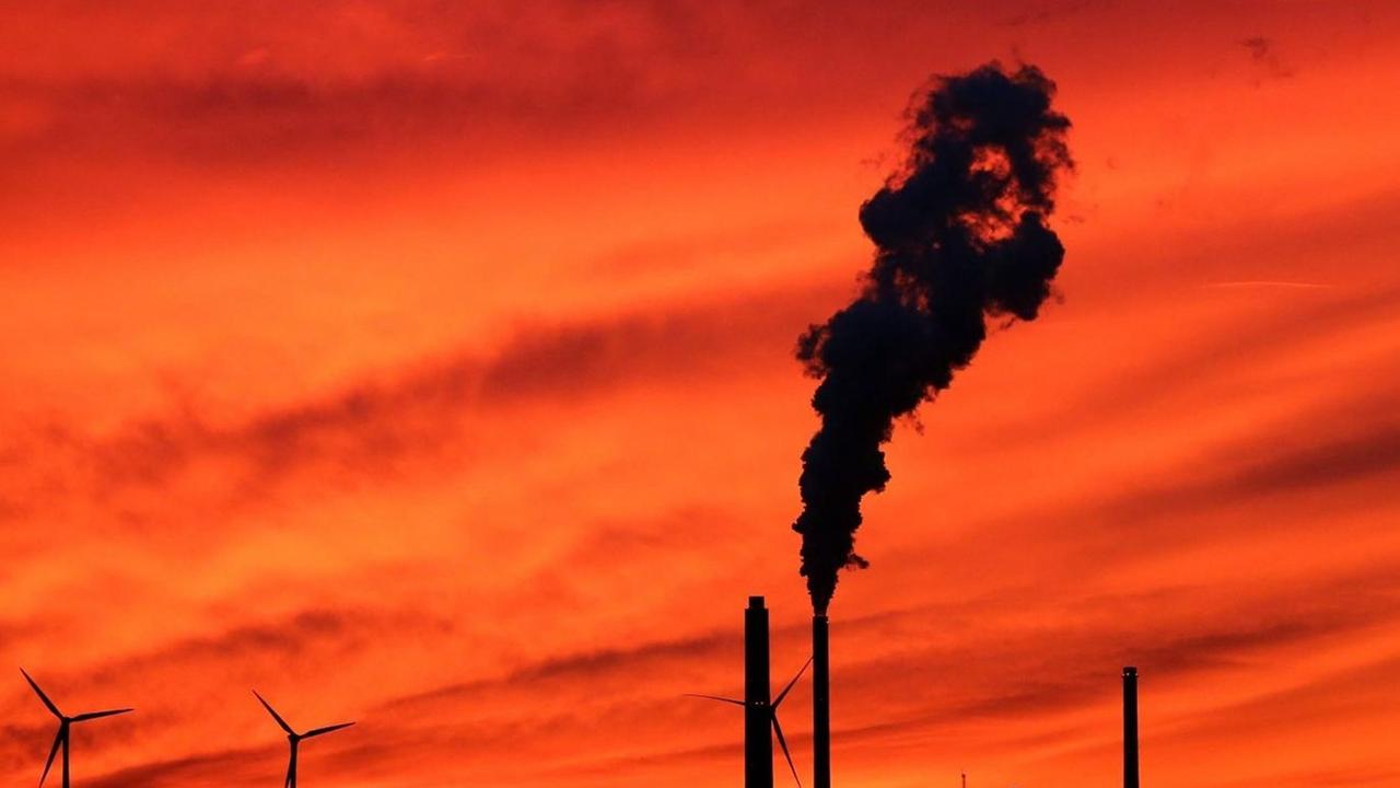 Blick in den Sonnenuntergangshimmel auf die Schornsteine des EnBW Dampfkraftwerkes und Windräder im Karlsruher Rheinhafen bei Sonnenuntergang.