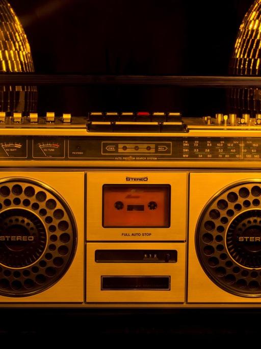 Ein Ghettoblaster steht vor zwei goldenen Discokugeln.