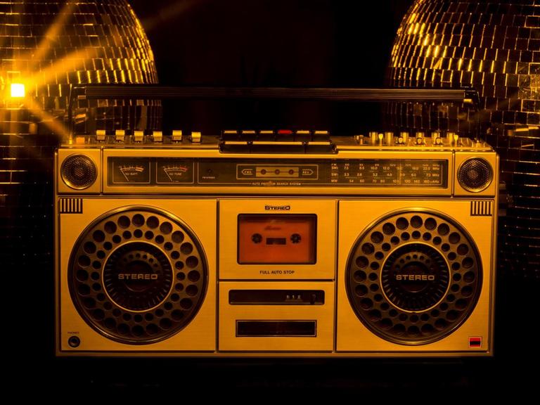 Ein Ghettoblaster steht vor zwei goldenen Discokugeln.