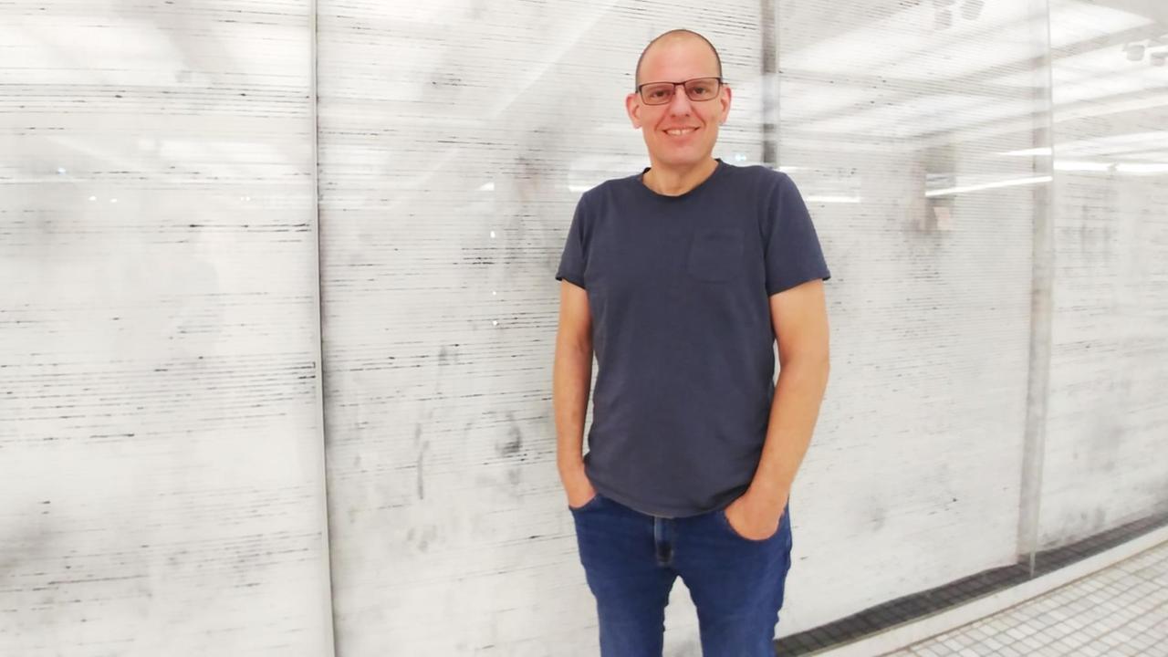 Hans Bernhard, Professor für Netz an der Kunsthochschule für Medien Köln, steht an einer Wand mit Wellenmuster im DLF-Funkhaus