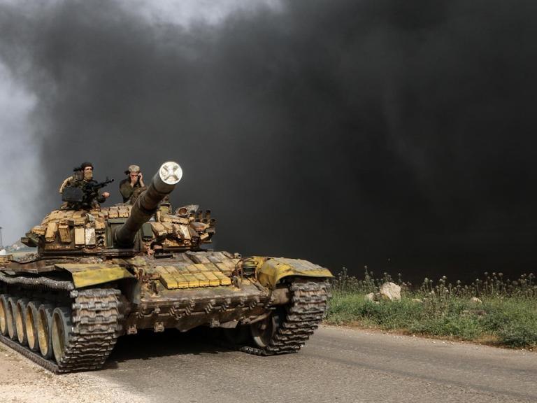 Syrien, Kafr Nabudah: Syrische Oppositionskämpfer fahren auf einer Straße mit einem Panzer an die Front in der Provinz Hama.