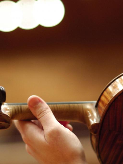 Hand einer Geigerin auf dem Hals einer Geige von hinten fotografiert