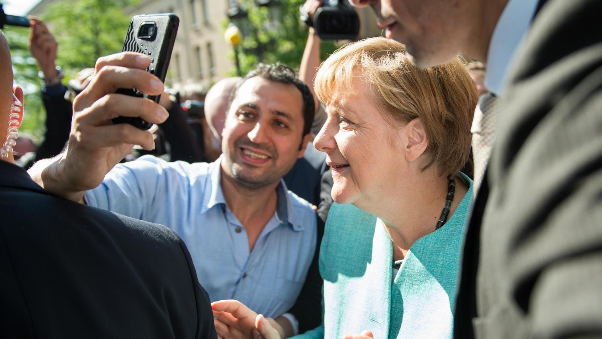 Bundeskanzlerin Merkel posiert in Berlin-Spandau mit einem Flüchtlinge für ein Selfie. Beide sind von Menschen umringt.