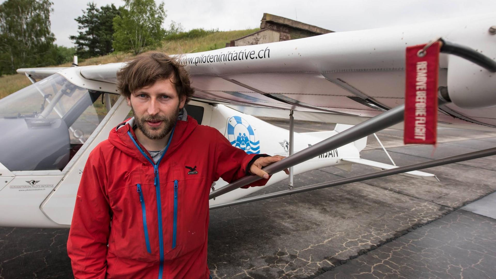 Der Pilot Ruben Neugebauer steht in roter Jacke vor einem Ultraleichtflugzeug.