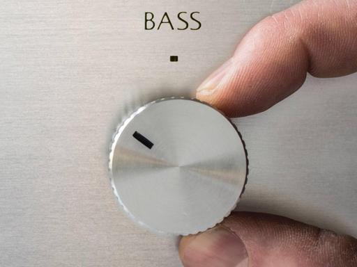 Eine Hand dreht am Bass-Regler einer Musikanlage