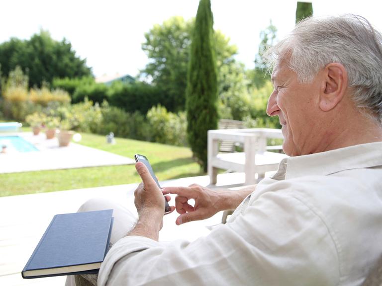 Ein Mann sitzt im Garten mit seinem Smartphone.