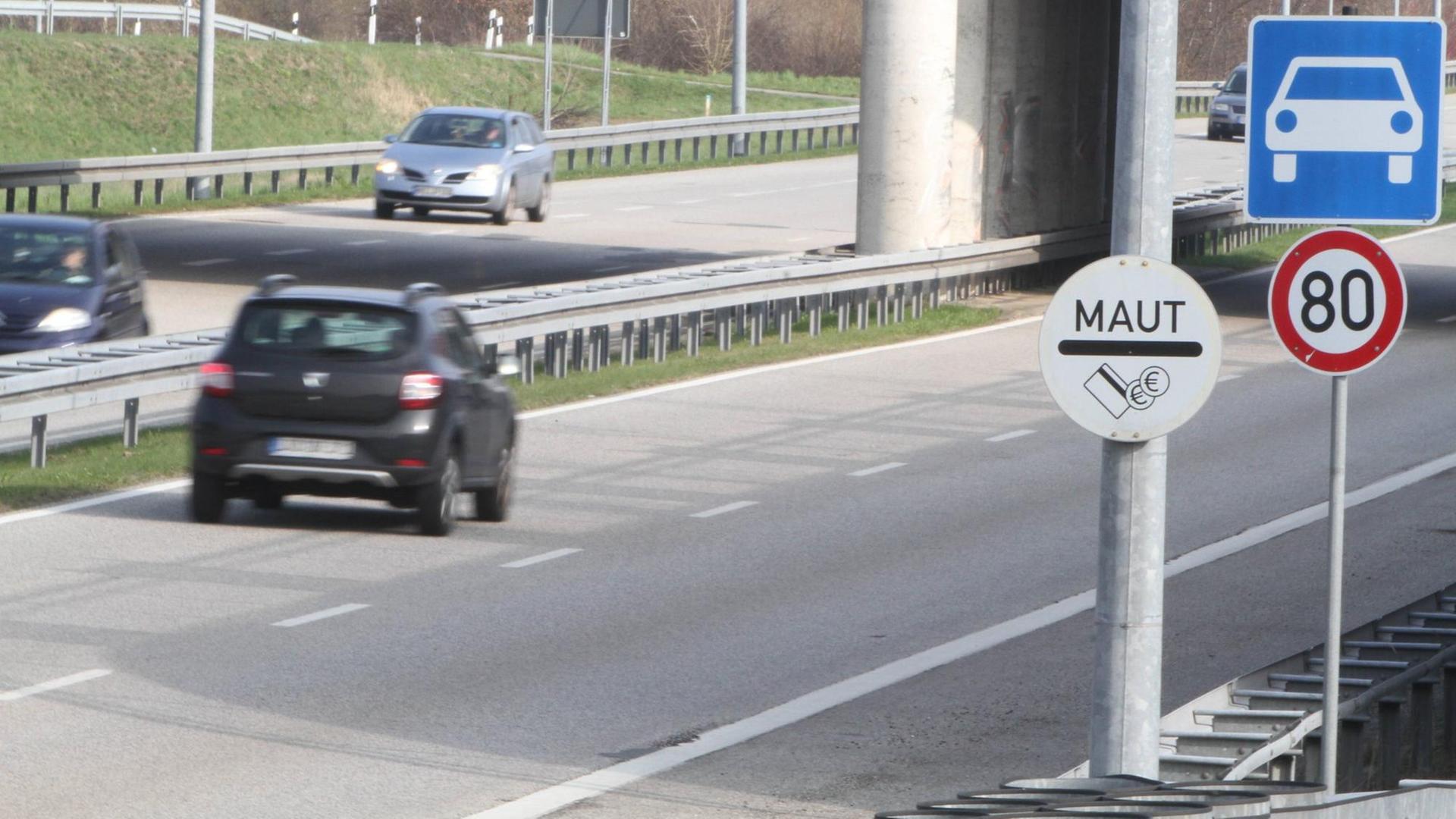 Eine mautpflichtige Straße in Rostock, darauf ein schwarzes Auto, am Straßenrand ein Schild mit der Aufschrift Maut und ein Hinweisschild "Autobahn".