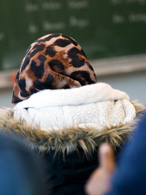 Eine Schülerin trägt im Klassenzimmer während des Unterrichtes eine Jacke und ein Kopftuch.