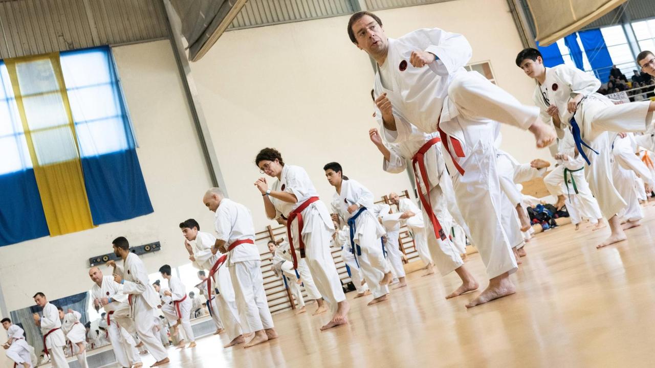 Ein Karate Event in Okinawa: In einer Turnhalle stehen dutzende Karatemeister in weißen Karateanzügen in Reihen.