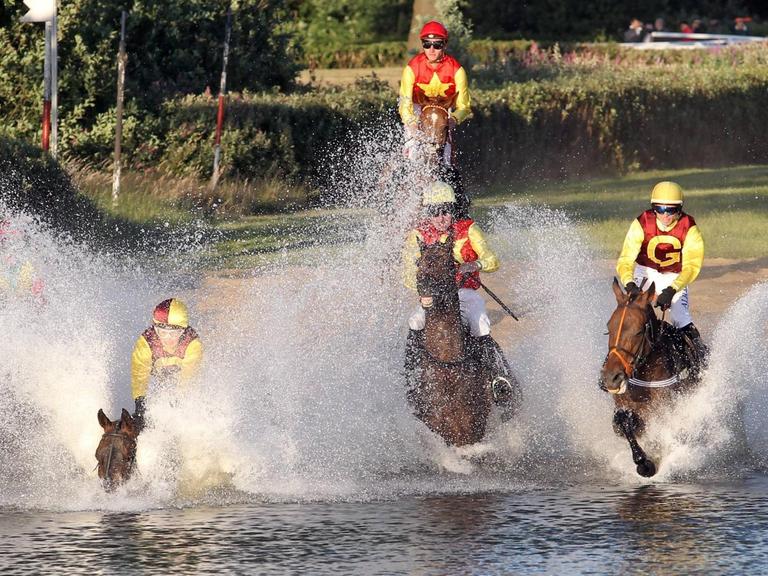 Pferde und Jockeys galloppieren im vollen Tempo in das Wasser während des Seejagdrennens auf der Galopprennbahn in Hamburg-Horn.