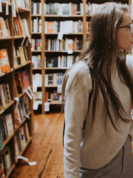 Eine junge Frau steht zwischen Bücherregalen in einem Buchladen und stöbert.