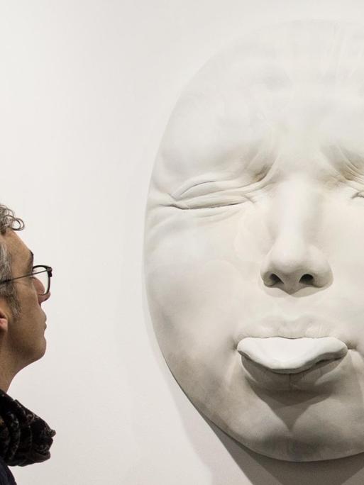 Der spanische Künstler Samuel Salcedo vor der, von ihm geschaffenen Plastik eines hyperrealistischen Gesichts, mit herausgestreckter Zunge.