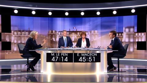 Marine Le Pen und Emmanuel Macron sitzen sich in einem Fernsehstudio an einem runden Tisch gegenüber. Dazwischen die beiden Moderatoren.