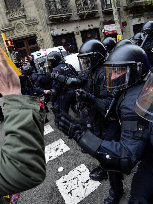 Demonstranten mit katalanischer Fahne stehen bewaffneten Polizisten mit Helmen gegenüber