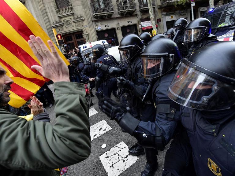 Demonstranten mit katalanischer Fahne stehen bewaffneten Polizisten mit Helmen gegenüber