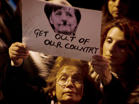 Eine Demonstrantin hält während einer Demonstration gegen das geplante Rettungspaket am 27.03.2013 in Nikosia, Zypern ein Bild von Angela Merkel mit angemaltem Hitlerbart in die Höhe.