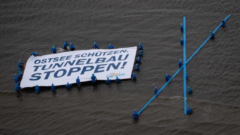 Demonstrierende mit einem Banner im Wasser, auf dem "Ostsee schützen. Tunnelbau stoppen!" steht