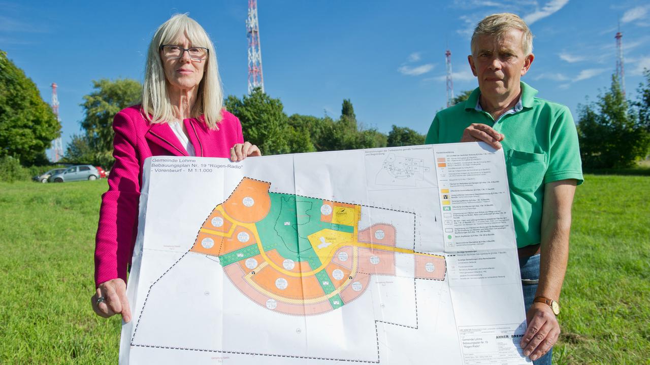 Die Mitglieder der Bürgerinitiative "Lohme bewahren", Susanne Monz und Jörg Burwitz, zeigen vor den Antennenträger der einstigen Sendestelle der Küstenfunkstelle "Rügen Radio" in Lohme den Bebauungsplan für die Immobilie.