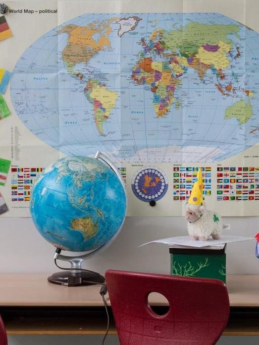 Eine Schulbank mit einem Globus, im Hintergrund eine Weltkarte.