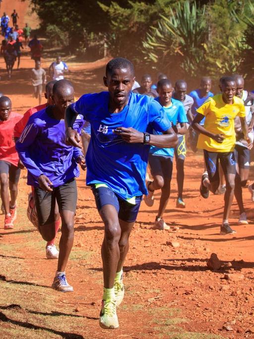 Junge Läufer sind auf einer Straße im roten Sand rund um die Kleinstadt Iten im hügeligen Hochland Kenias unterwegs