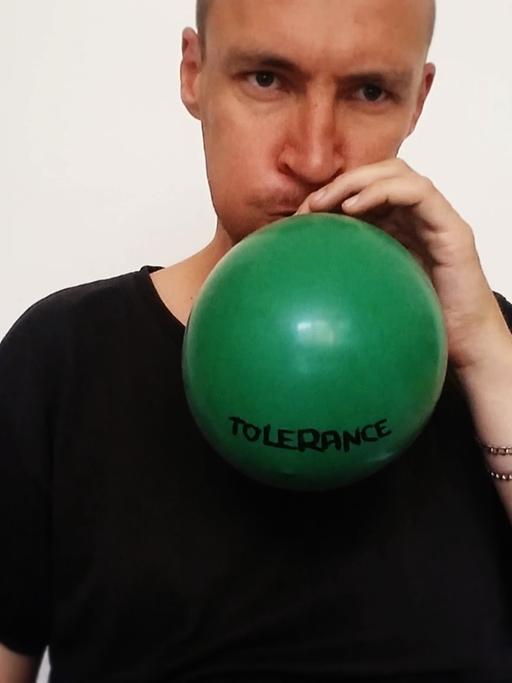 Der Audio- und Videokünstler Kuesti Fraun bläst einen grünen Luftballon auf mit der Beschriftung "Tolerance"