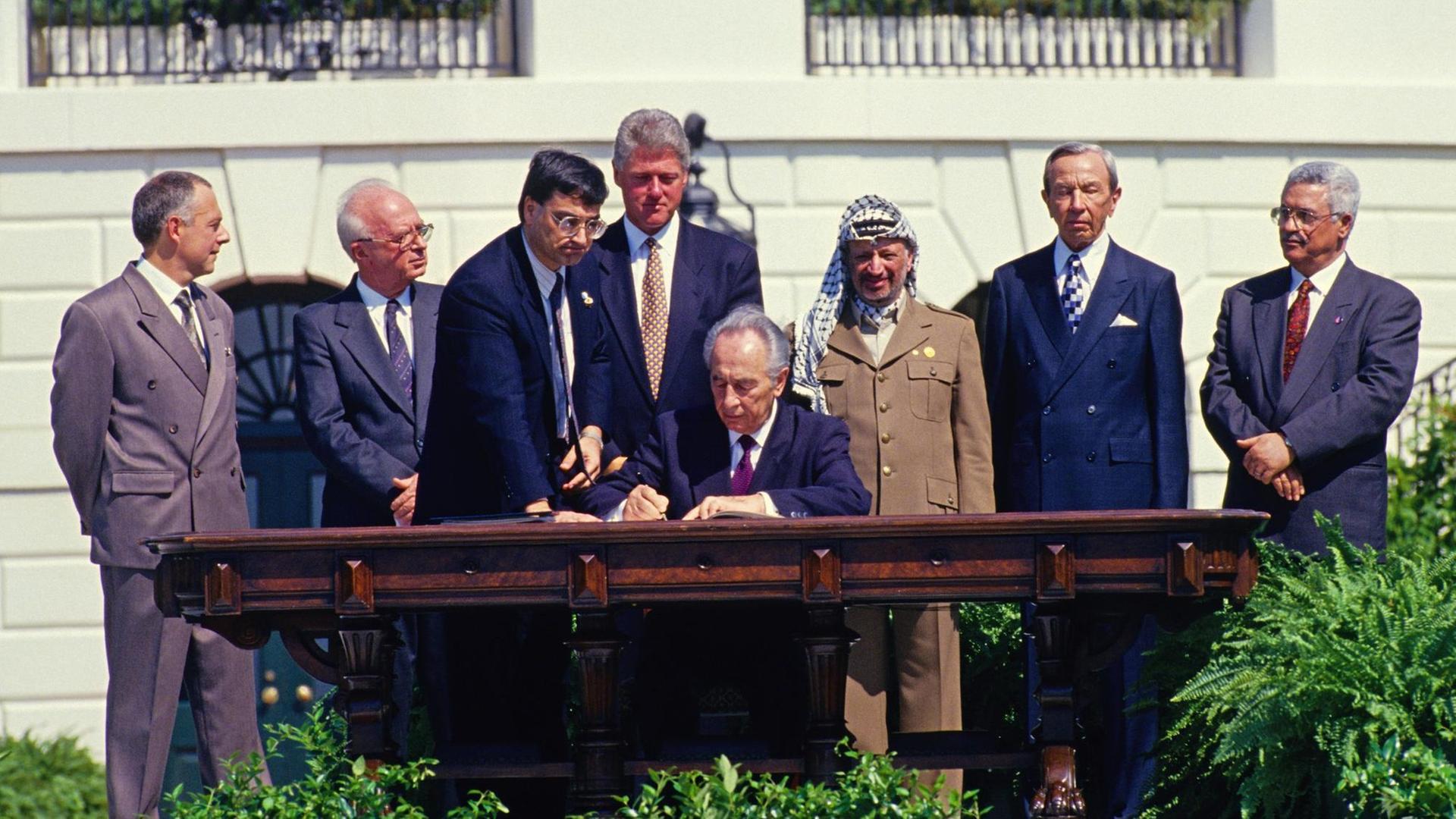 Shimon Peres setzt am 13. September 1993 in Washington seine Unterschrift unter das Abkommen von Oslo, hinter ihm stehen u.a. der israelische Premierminister Jitzhak Rabin, PLO-Chef Jassir Arafat und US-Präsident Bill Clinton.