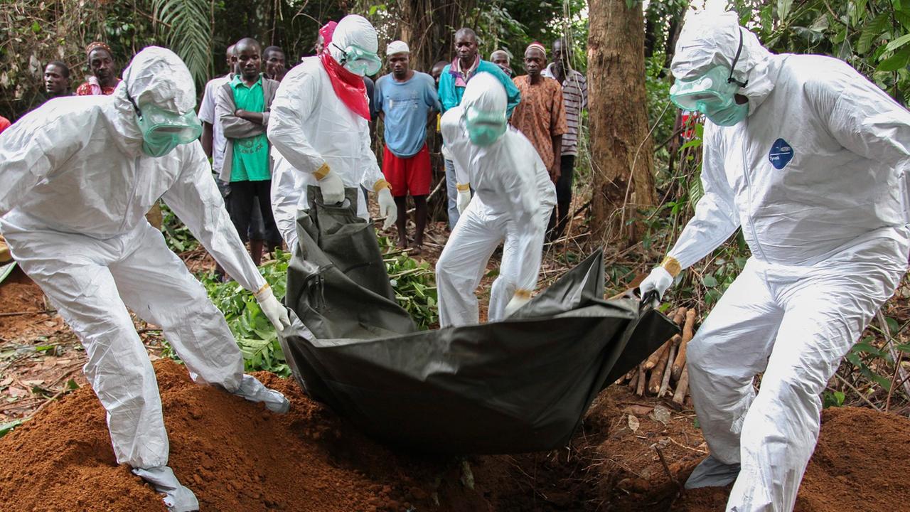 Ein Mensch, der an Ebola gestorben ist, wird von Helfern in Schutzanzügen beerdigt.