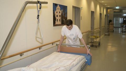 Ein junger Mann schiebt in einem Krankenhaus ein Bett durch den Flur.