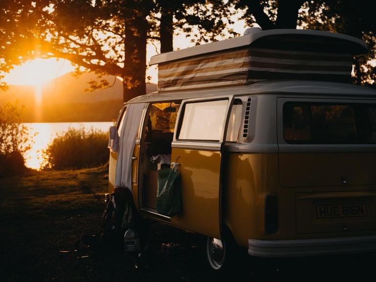 Ein Wohnwagen steht bei Sonnenuntergang an einem See.