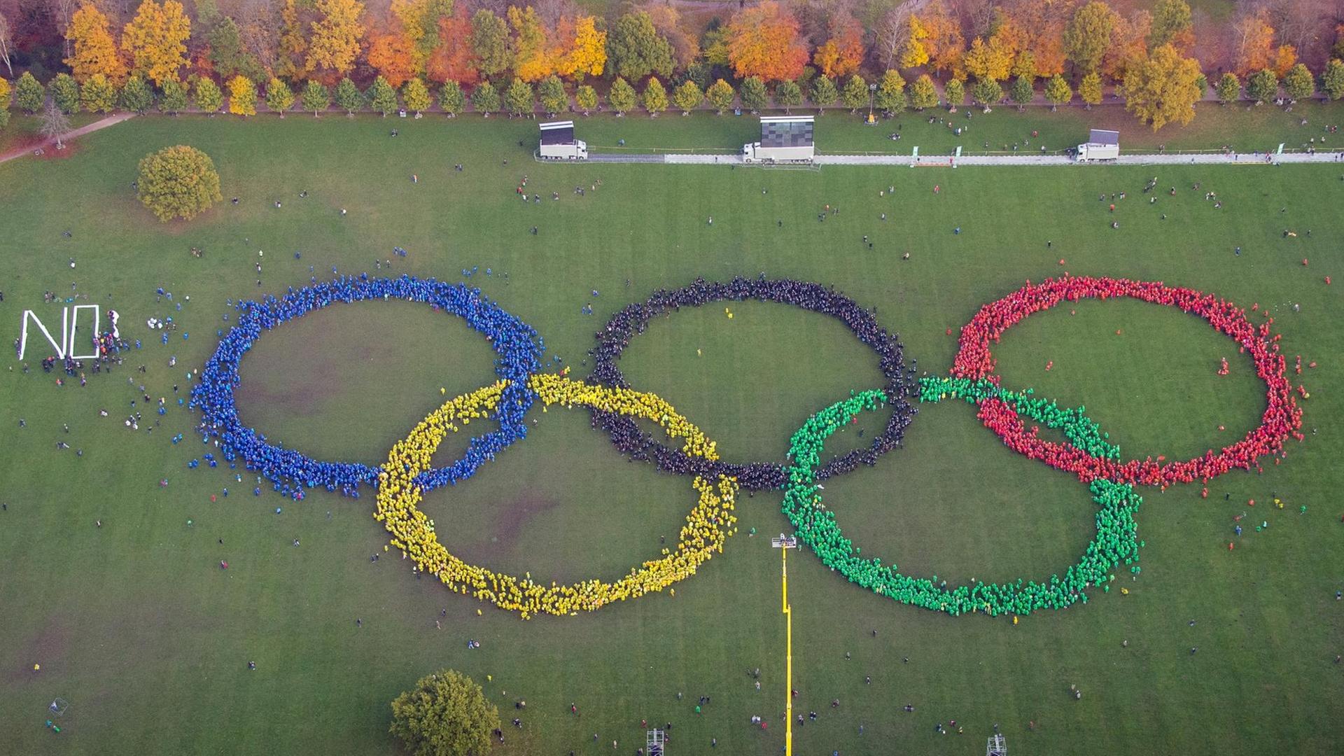 Hunderte Menschen in bunten Ponchos bilden im Stadtpark in Hamburg die Olympischen Ringe. Gegner haben davor das Wort "No" gebildet.