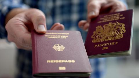 Eine Hand hält einen britischen und ein deutschen Reisepass in die Kamera.