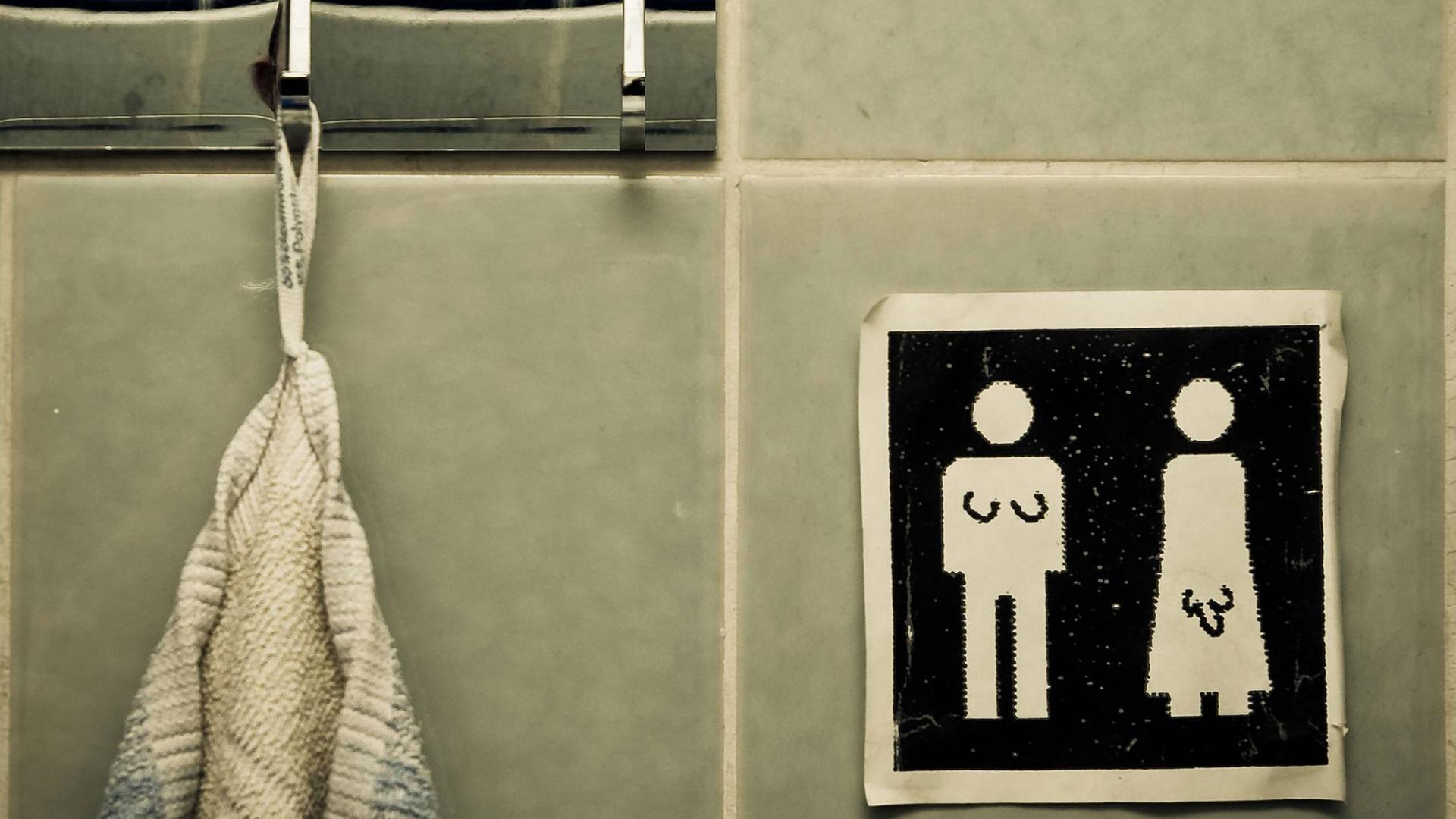 Unisex Handtuch. Symbole auf einem Schild: Für Männer und Frauen. Jemand hat signifikante Körpermerkmale für Transgender People ergänzt.
