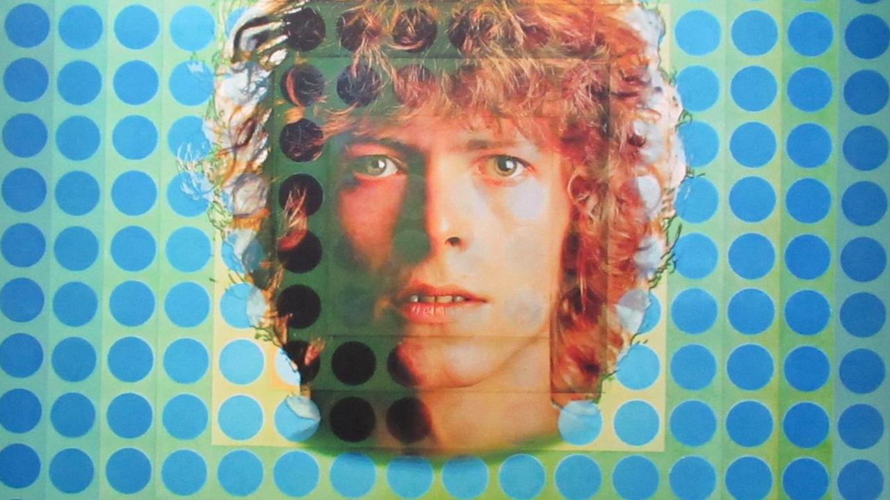 Zu sehen ist ein Ausschnitt des Plattencovers des Albums «Space Oddity». Es wurde vom Künstler Victor Vasarely im quadratischem Format gestaltet und besteht aus Punkten in unterschiedlichen Blautönen. In der Bildmitte das prägnante Gesicht von David Bowie mit lockigem, rötlichem Haar.