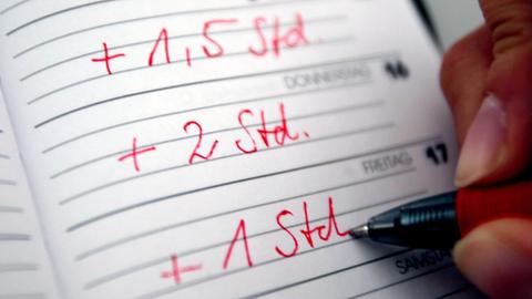 Jemand trägt seine Überstunden mit rotem Stift in einen Taschenkalender ein.
