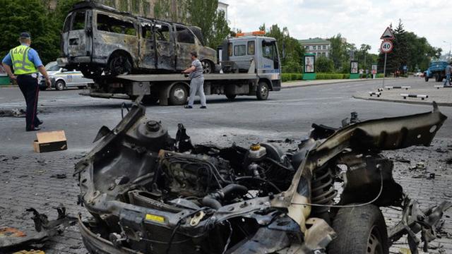 Arbeiter schleppen in der ost-ukrainischen Stadt Donezk einen ausgebrannten Minibus ab, der durch eine Explosion neben einem ebenfalls ausgebrannten Auto zerstört wurde.