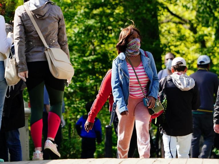 Menschen gehen mit Mund- und Nasenschutz im Central Park spazieren.